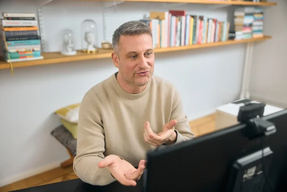Ein Mann sitzt vor einem Rechner mit Webcam und spricht