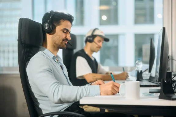 Zwei Männer mit Headsets sitzen konzentriert vor ihren PCs