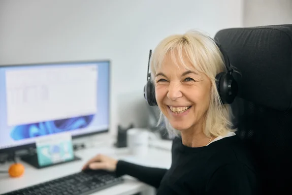 Eine lachende Frau mit Headset am Schreibtisch