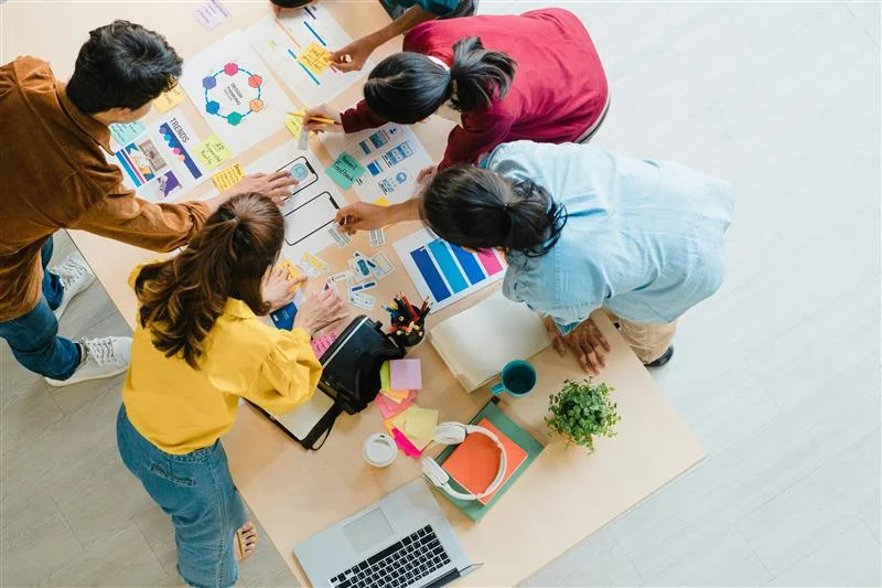 Blick von oben auf fünf Marketing-Mitarbeiter über einem Tisch mit bunten Statistiken.