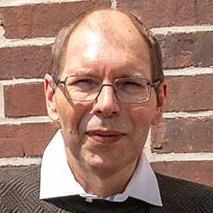 Der erfolgreiche Umschüler André Pardun steht mit verschränkten Armen vor einer geziegelten Hauswand.