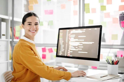 eine Frau, die an einem Schreibtisch mit einem Computer sitzt und mit einer anderen Frau spricht