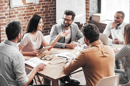 eine Gruppe von Menschen, die um einen Tisch sitzen und zwei Männer die Hände schütteln