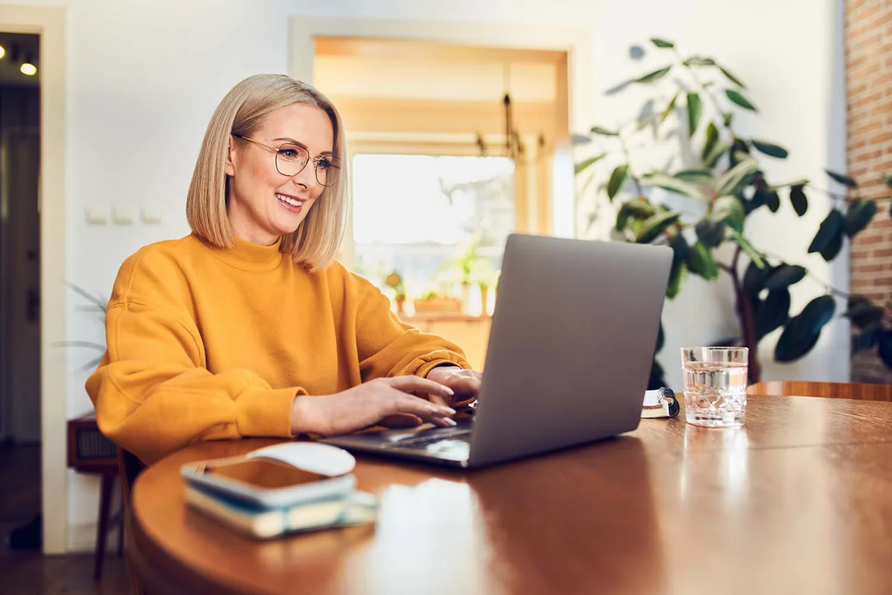 eine Frau sitzt an einem Tisch mit einem Laptop vor orangenem Hintergrund