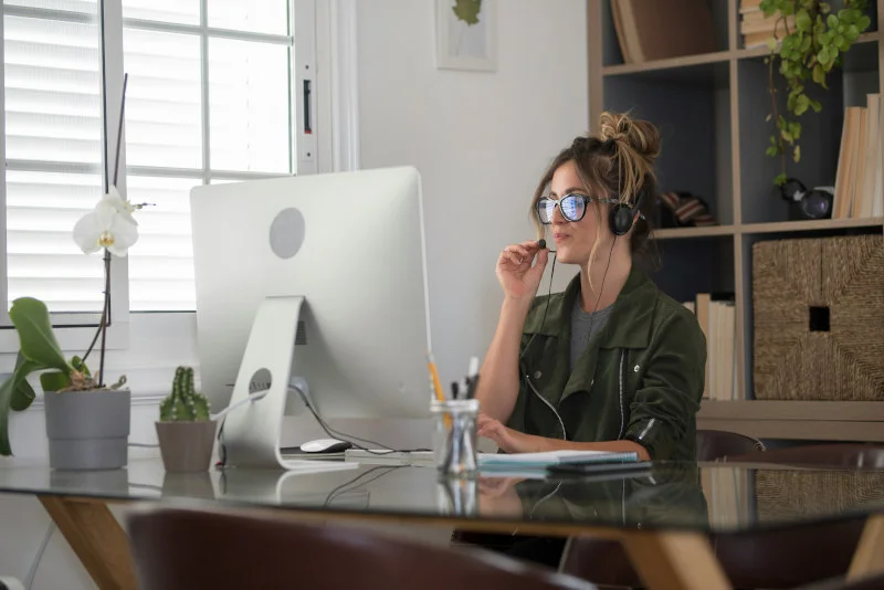 Junge Frau mit Brille sitzt in ihrem modernen Arbeitszimmer am Schreibtisch und nimmt an ihrer Online-Weiterbildung teil.