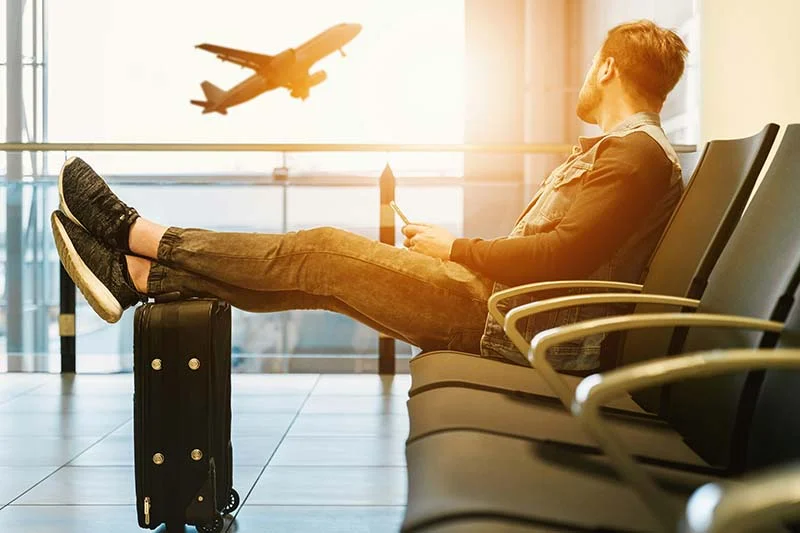 Mann sitzt, Füße auf dem Koffer, in der Flugzeug-Wartehalle.