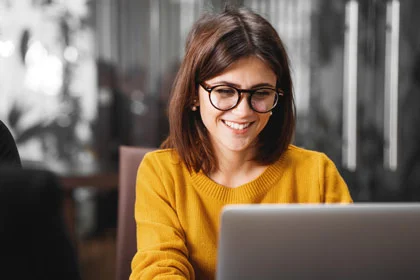 eine Frau sitzt an einem Tisch mit einem Laptop vor orangenem Hintergrund