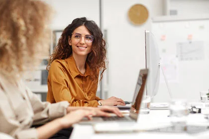 zwei Frauen sitzen an einem Schreibtisch mit einem Computer