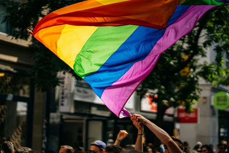 Regenbogenflagge wird über den Köpfen von marschierenden Menschen geschwenkt.