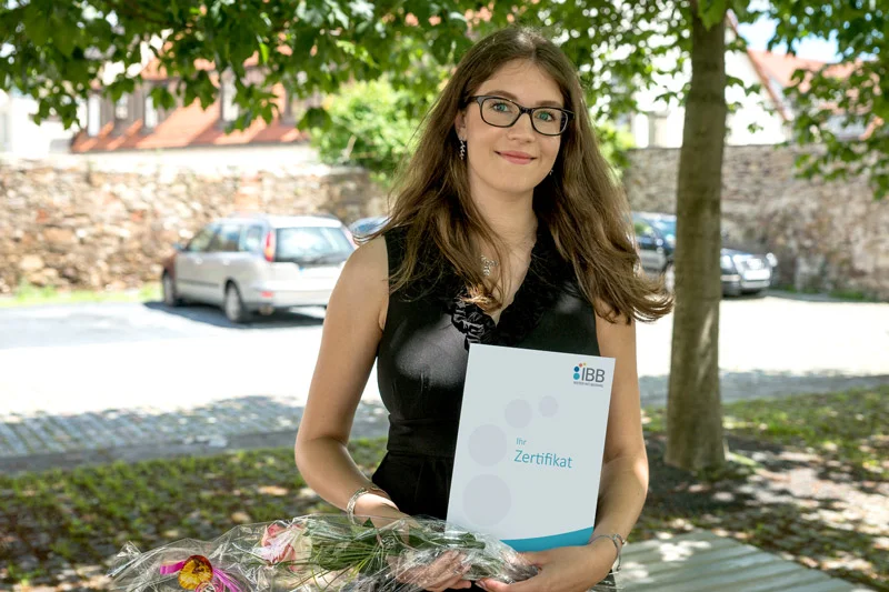 Junge Frau hält ein IBB-Zertifikat und Blumen in der Hand.