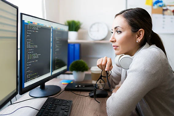 eine Frau, die an einem Schreibtisch mit einem Computer sitzt und mit einer anderen Frau spricht