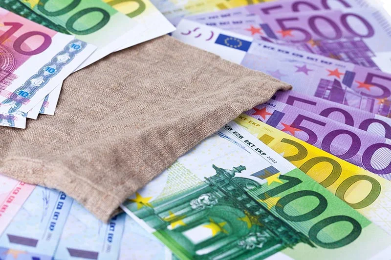 Eine Bündel verschiedener Euroscheine liegen in, neben und unter einem kleinem Stoffbeutel.